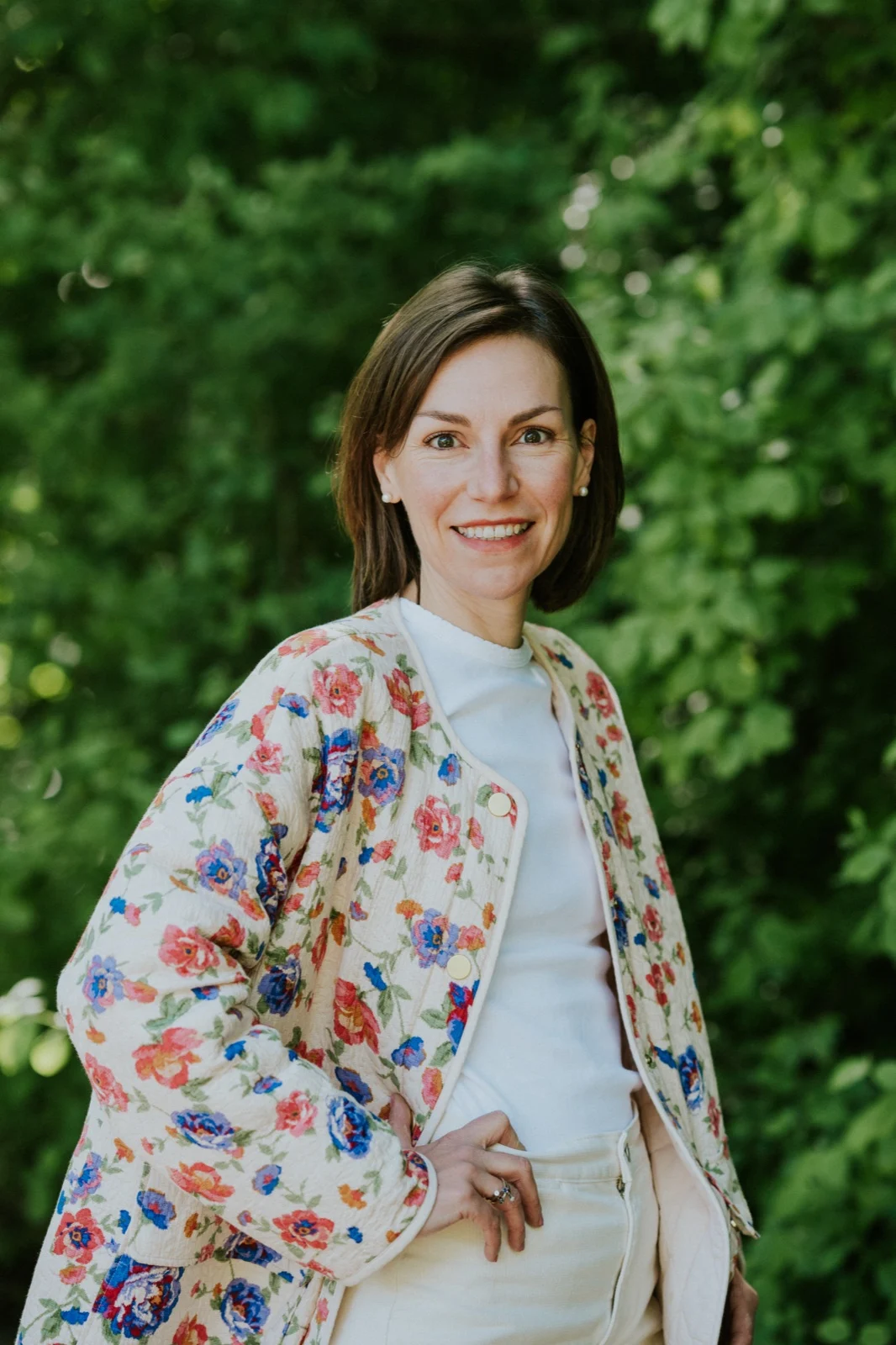 Portrait d'Aude Roposte, souriante, en veste fleurie devant un feuillage